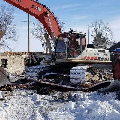 Excavator clearing debris in a snowy demolition site.