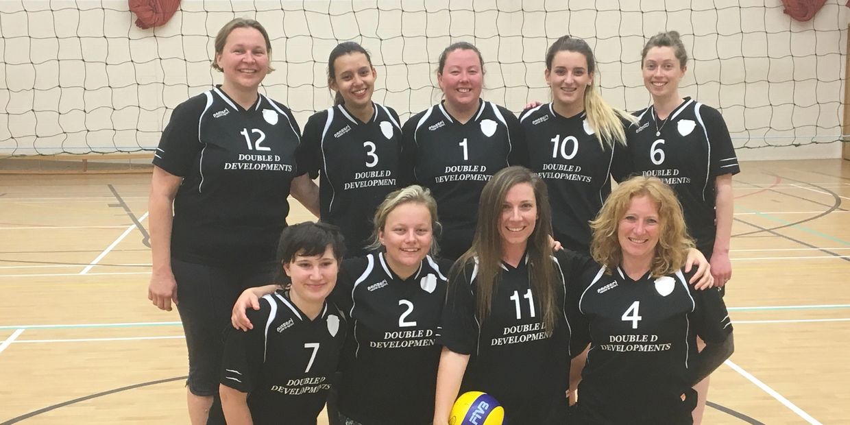 A smiling women's volleyball team posing on an indoor court.