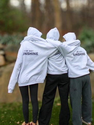 Three people wearing matching gray hoodies outdoors.