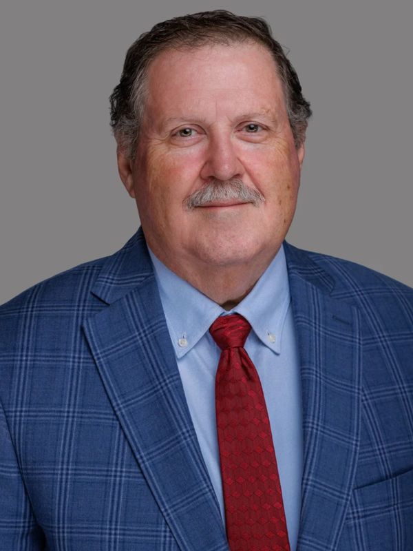 Middle-aged man in a blue plaid suit and red tie against a gray backdrop.