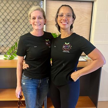 Two women wearing matching black T-shirts with a heart logo, smiling indoors.
