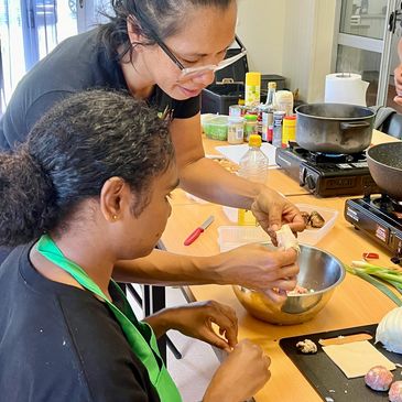 Two women cooking together, one teaching the other how to wrap food.
