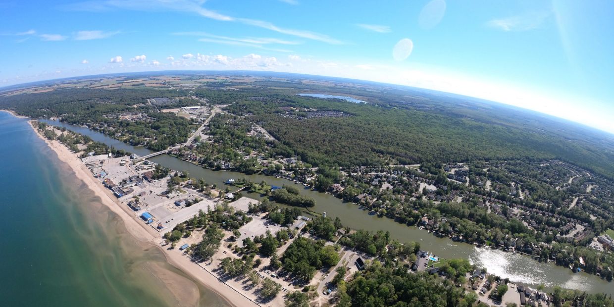Aerial view of a coastal town with a river, beach, and greenery under a clear blue sky.