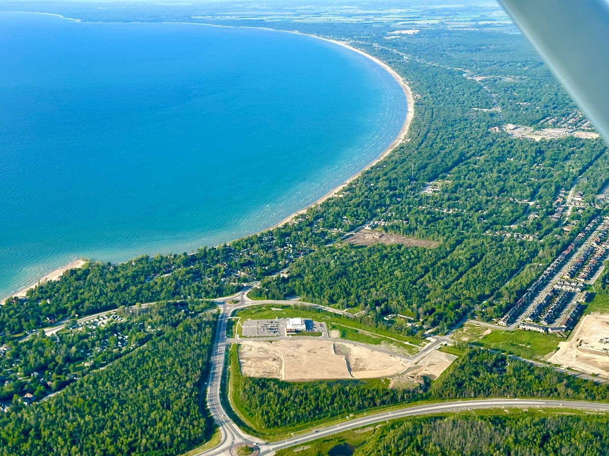 Aerial view of a large curved beach adjoining a green forest and residential area.