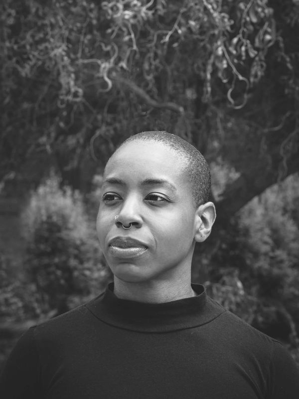 headshot of person looking towards the left wearing a turtle neck shirt, background of tree/foliage