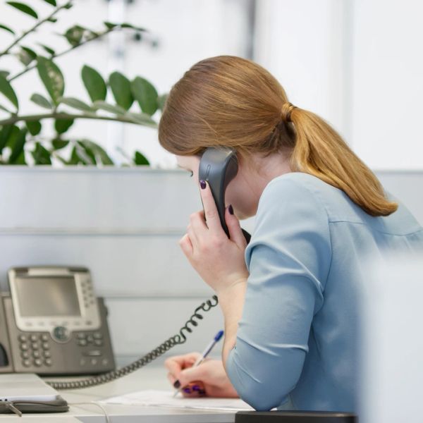 Frau am Schreibtisch telefoniert und macht Notizen.