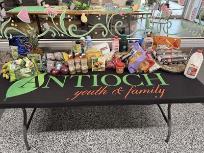 A table with various groceries displayed on an Antioch Youth &amp; Family cloth.