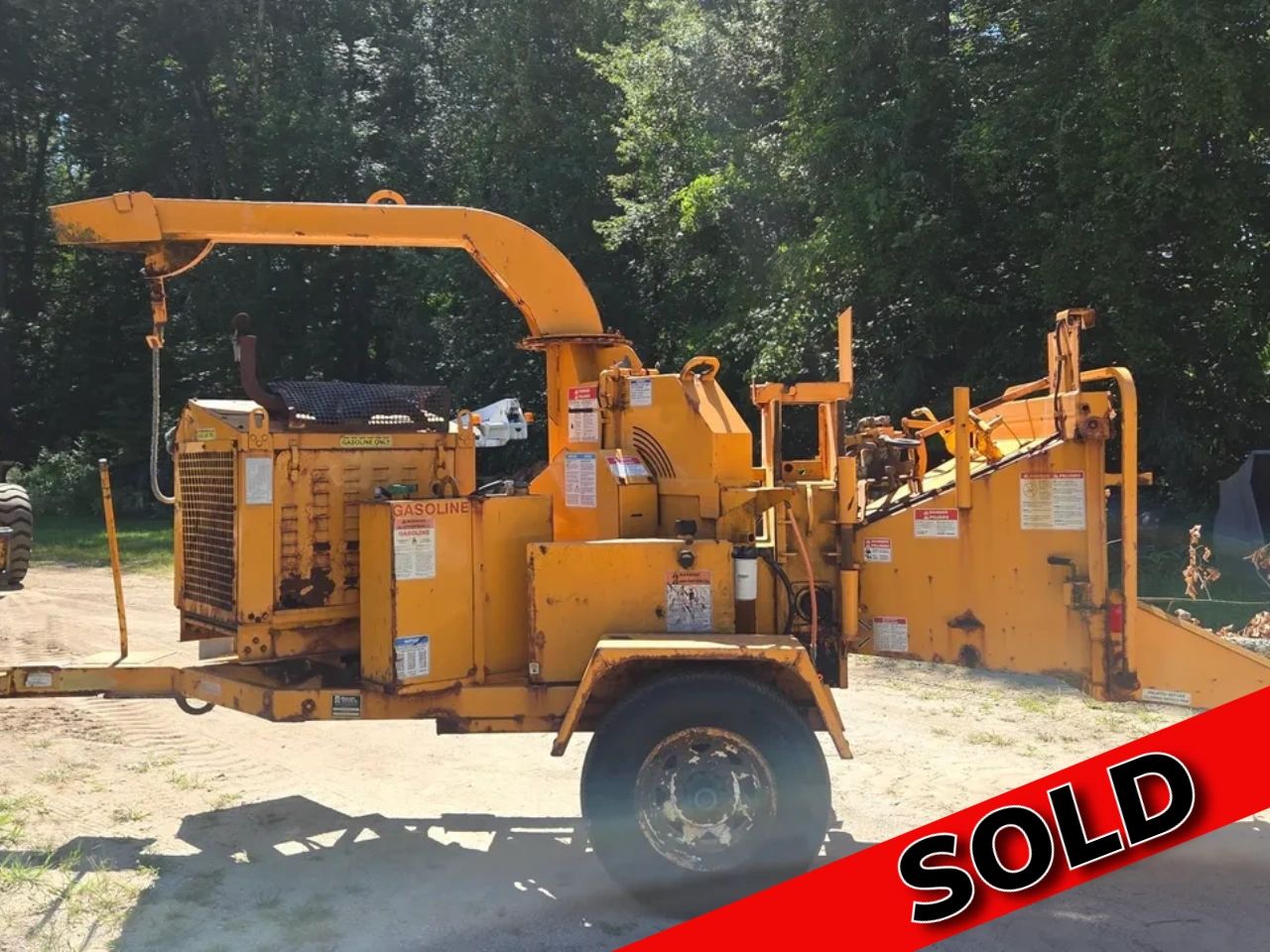 Yellow wood chipper machine outdoors with SOLD banner.