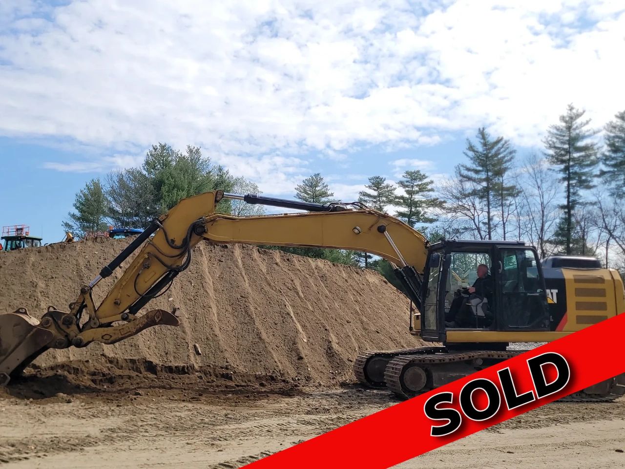 A yellow excavator at a construction site with a red SOLD banner.