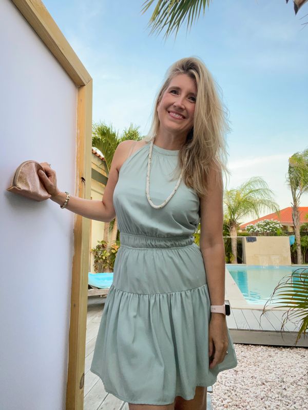 Smiling woman in a light green dress by a pool on a sunny day.