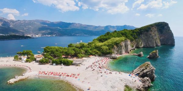 Scenic beach with clear waters, rocky cliffs, and sunbathers under a blue sky.