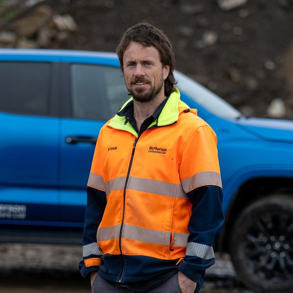 Man in high-visibility jacket standing by blue vehicle.