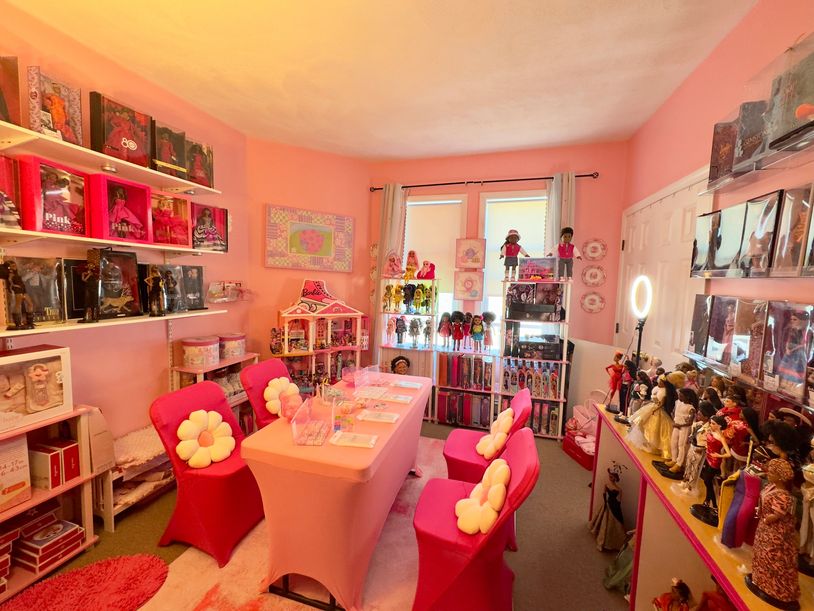 A vibrant pink room filled with doll collections and a table with pink chairs.