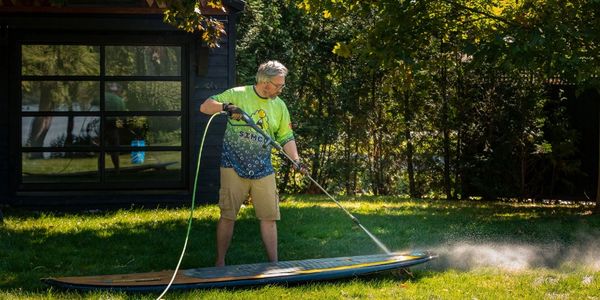 Man pressure washing surf board.