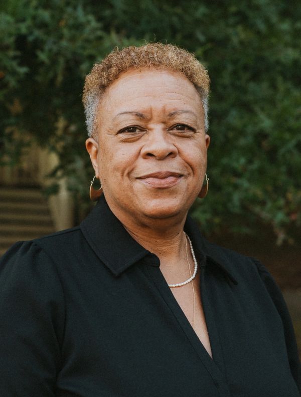 Confident middle-aged person with short curly hair, wearing black and smiling.