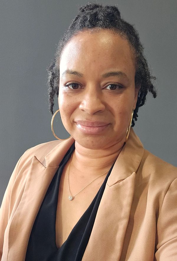 Woman with natural hair wearing a beige blazer and hoop earrings.