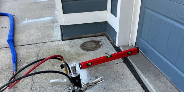 Concrete lifting equipment in use on a driveway with a level tool nearby.