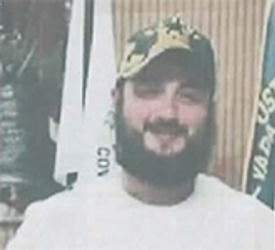 Man with a beard and camouflage cap smiling indoors.