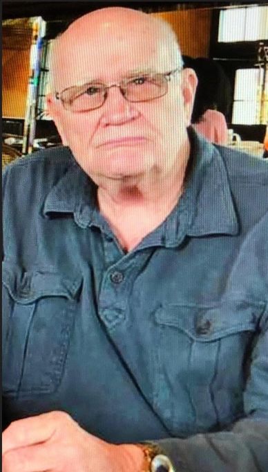 Elderly man with glasses in a casual shirt.