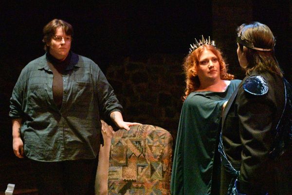 Three actors in a dramatic medieval-themed stage scene with crowns and cloaks.