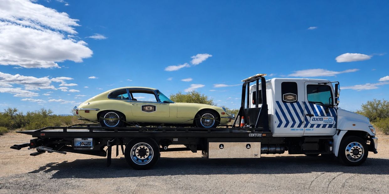 Classic car on a flatbed tow truck under blue sky.