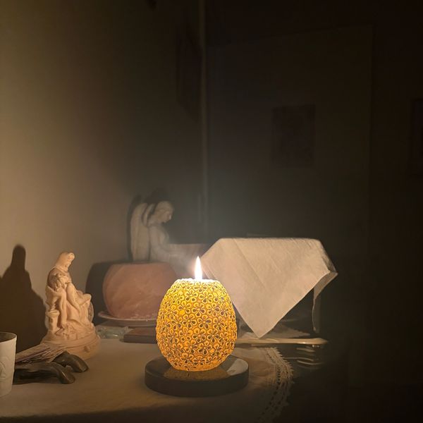 A glowing yellow candle illuminates a dimly lit room with statues and a table.