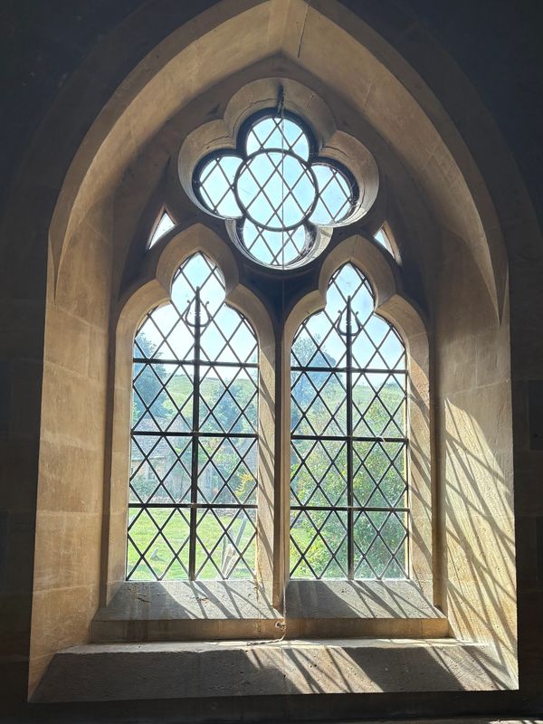 Sunlight streams through a gothic arched window with decorative panes.