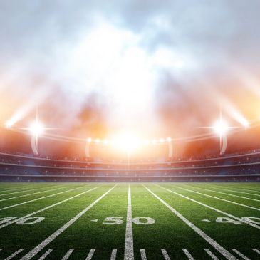 A bright, illuminated American football stadium at sunset.