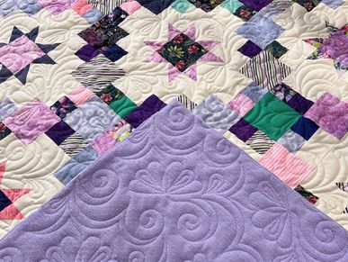 Colorful patchwork quilt with star patterns and purple fabric corner.