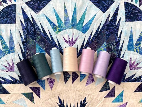 Seven colorful spools of thread on a patterned quilt.