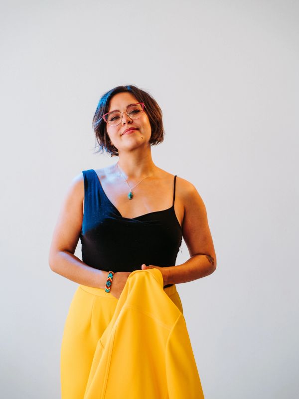 Woman in black top and yellow pants holding a yellow jacket.