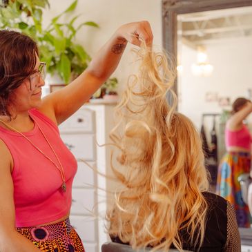 A hairstylist holding up blonde hair extensions in a salon.