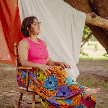 Woman in colorful skirt sitting on a wooden chair outdoors.