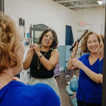 Two women enjoying hairstyling in a salon with smiles and laughter.