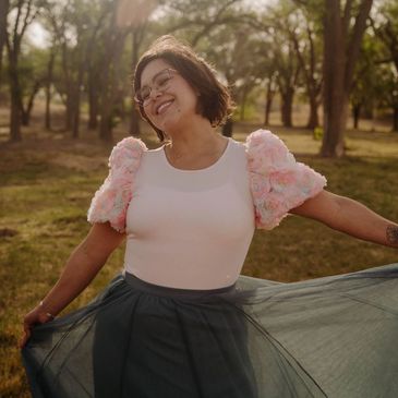 Woman joyfully posing outdoors with a flowy skirt and floral puff sleeves.