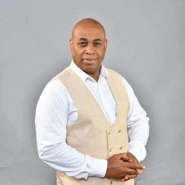 Man in white shirt and beige vest posing.