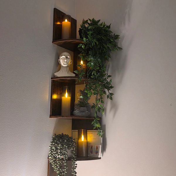 Corner wall shelf with candles, plants, and statues.