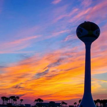 Silhouette of a water tower against a colorful sunset sky with palm trees.