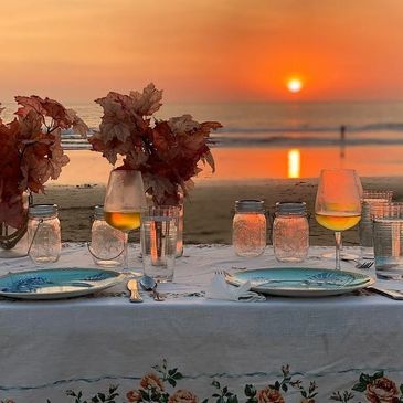 Elegant beachside dinner setup with sunset view and autumn leaves.