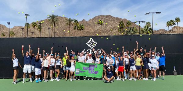 Group of tennis players tossing balls at Nike Tennis Camp in front of mountains.