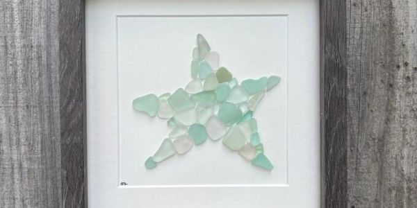 Sea glass pieces arranged in a star shape framed on a wall.