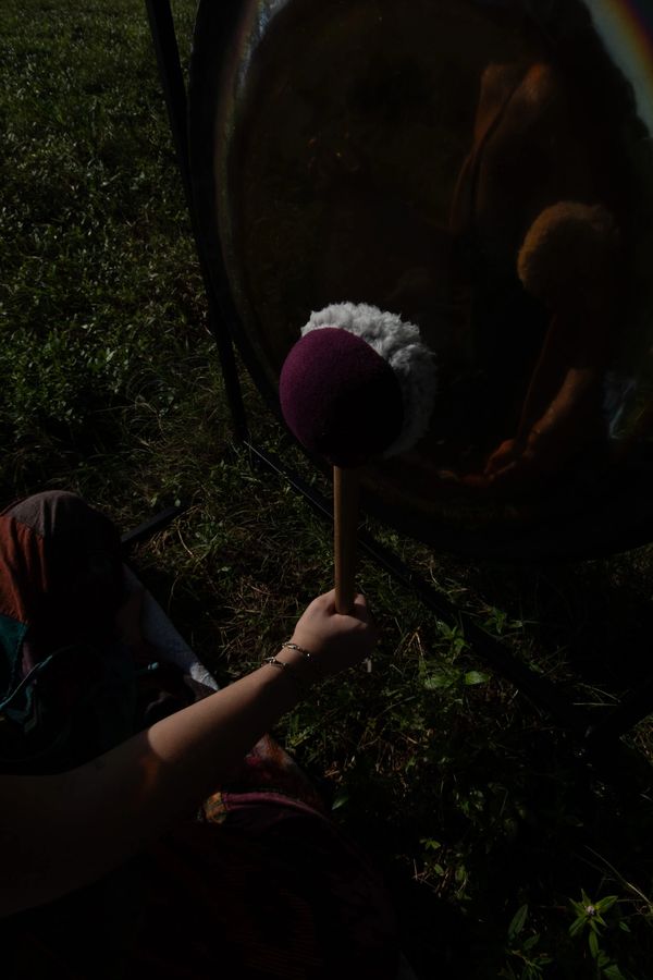 Hand holding a mallet poised to strike a large gong outdoors.