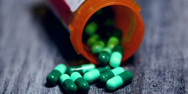 Green capsules spilling out of an orange prescription bottle on a dark surface.