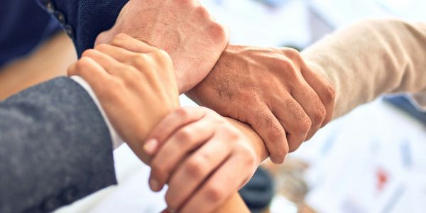 Four hands clasped together symbolizing unity and teamwork.