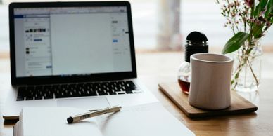 Workspace with a laptop, notebook, pen, and a coffee cup on a wooden table.