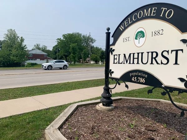 Welcome sign for Elmhurst with a road and car in the background.