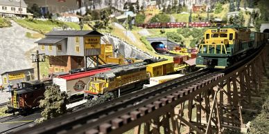 Detailed model train set with multiple locomotives and a mountainous backdrop.