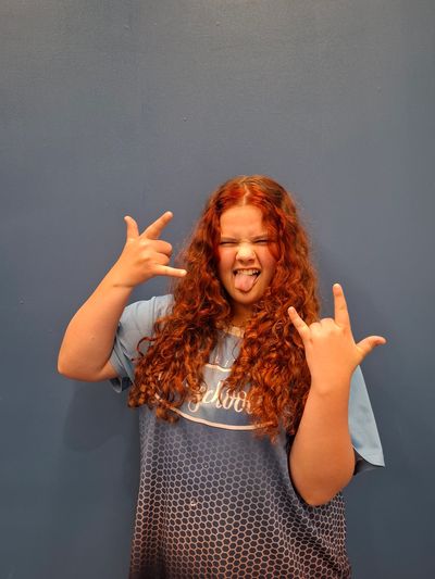 Girl with curly red hair making rock hand signs and sticking out her tongue.