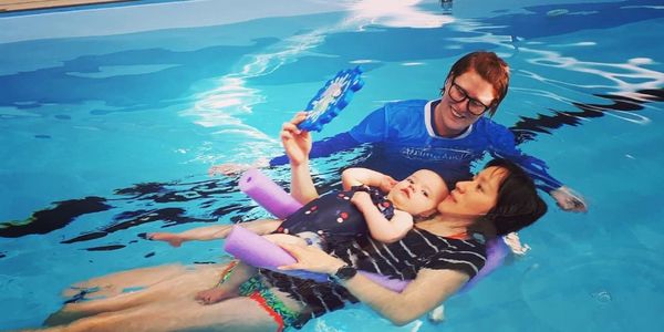 A dedicated swimming teacher working with a mother and her young baby