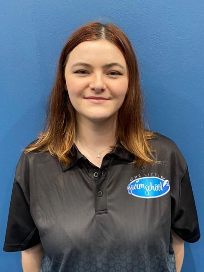 Young woman smiling wearing a black swim school polo shirt against a blue background.